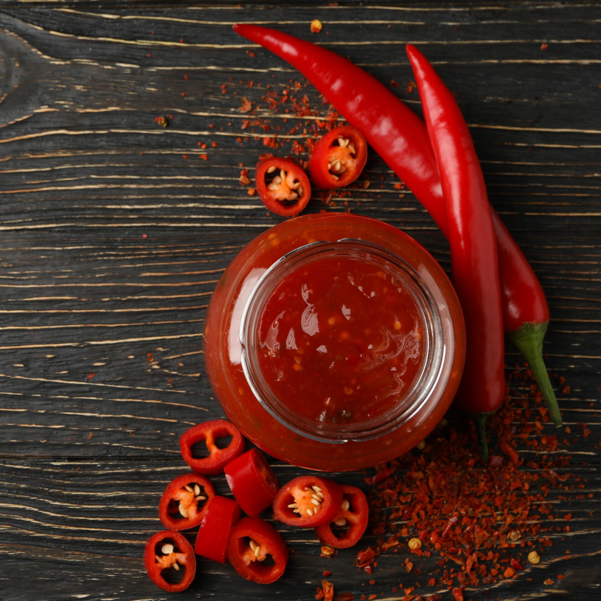 Chilli pepper and glass jar of sauce on wooden background, top view